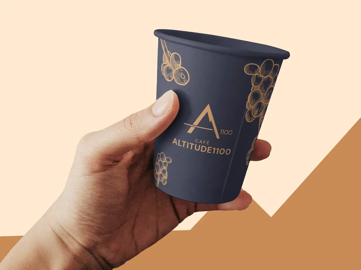 Mão segurando copo de papel azul-escuro com a marca Café Altitude 1100