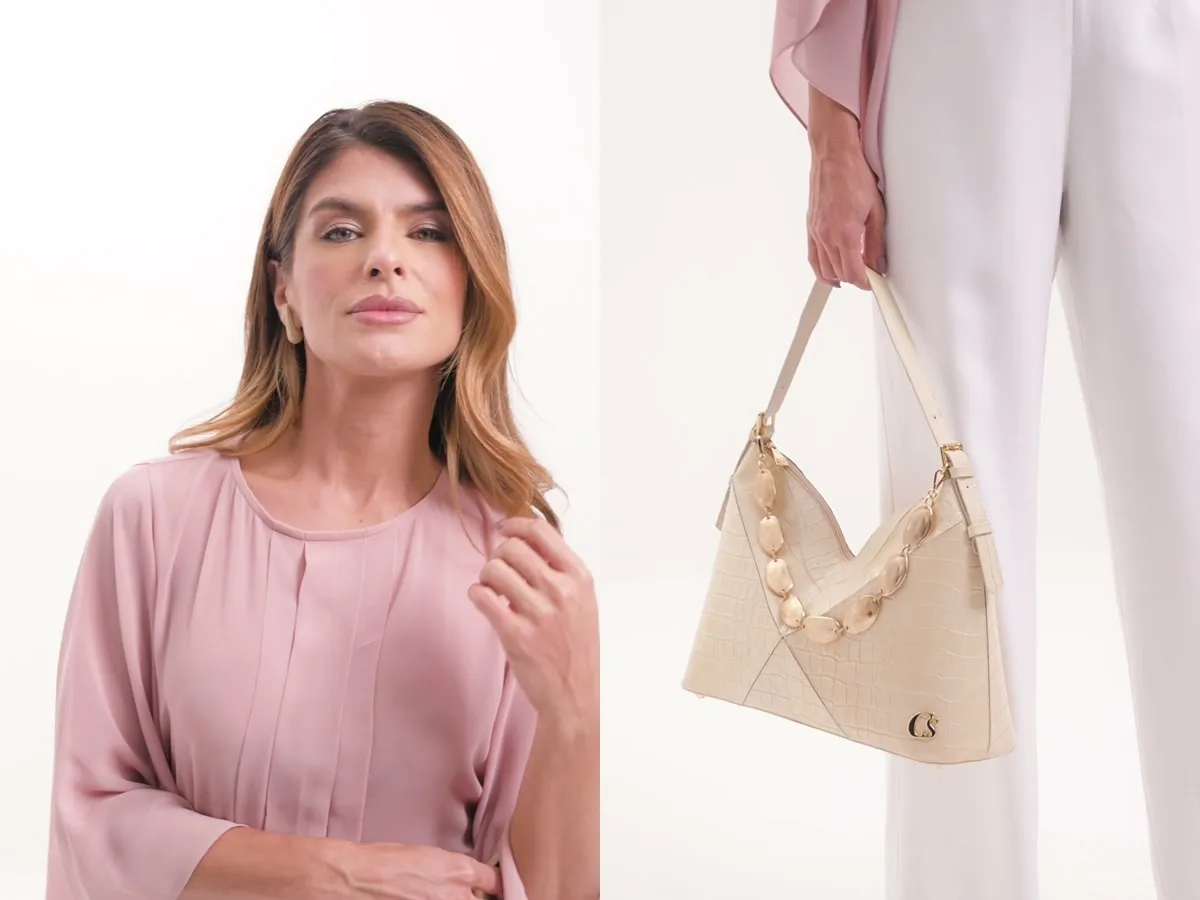 Modelo de blusa rosa e detalhe de bolsa clara com corrente dourada, em fundo branco