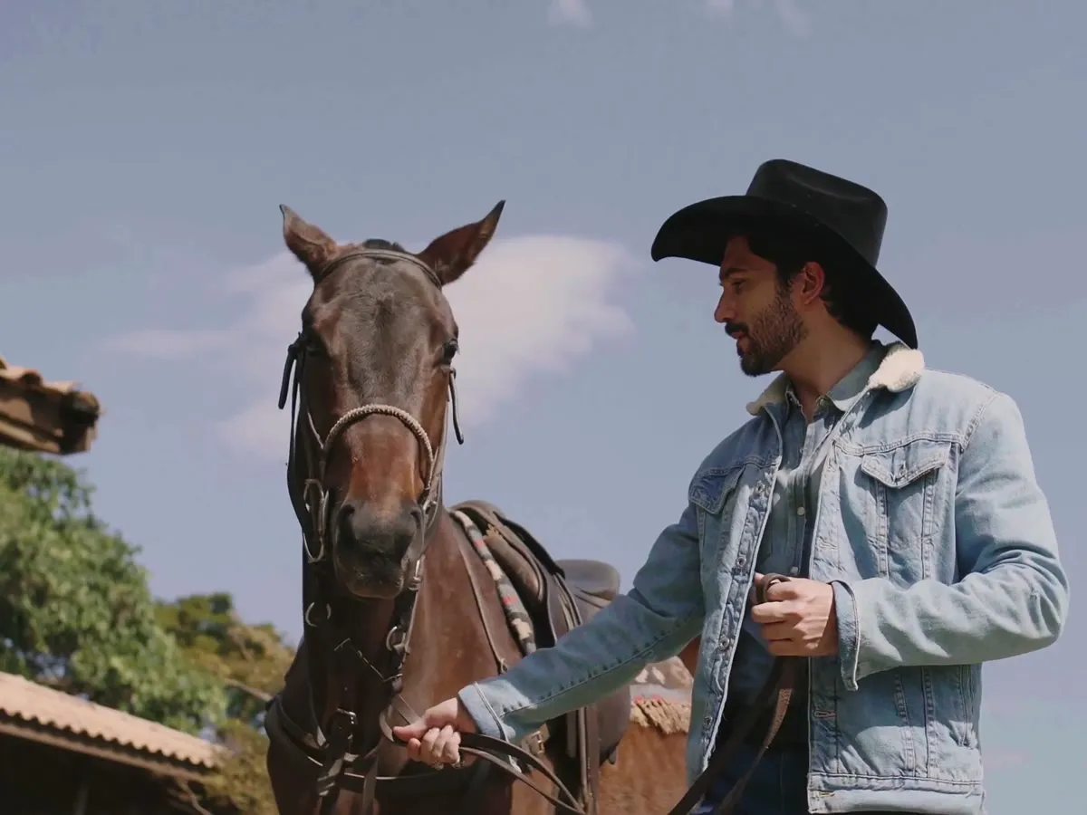 Homem de chapéu e jaqueta jeans conduz um cavalo