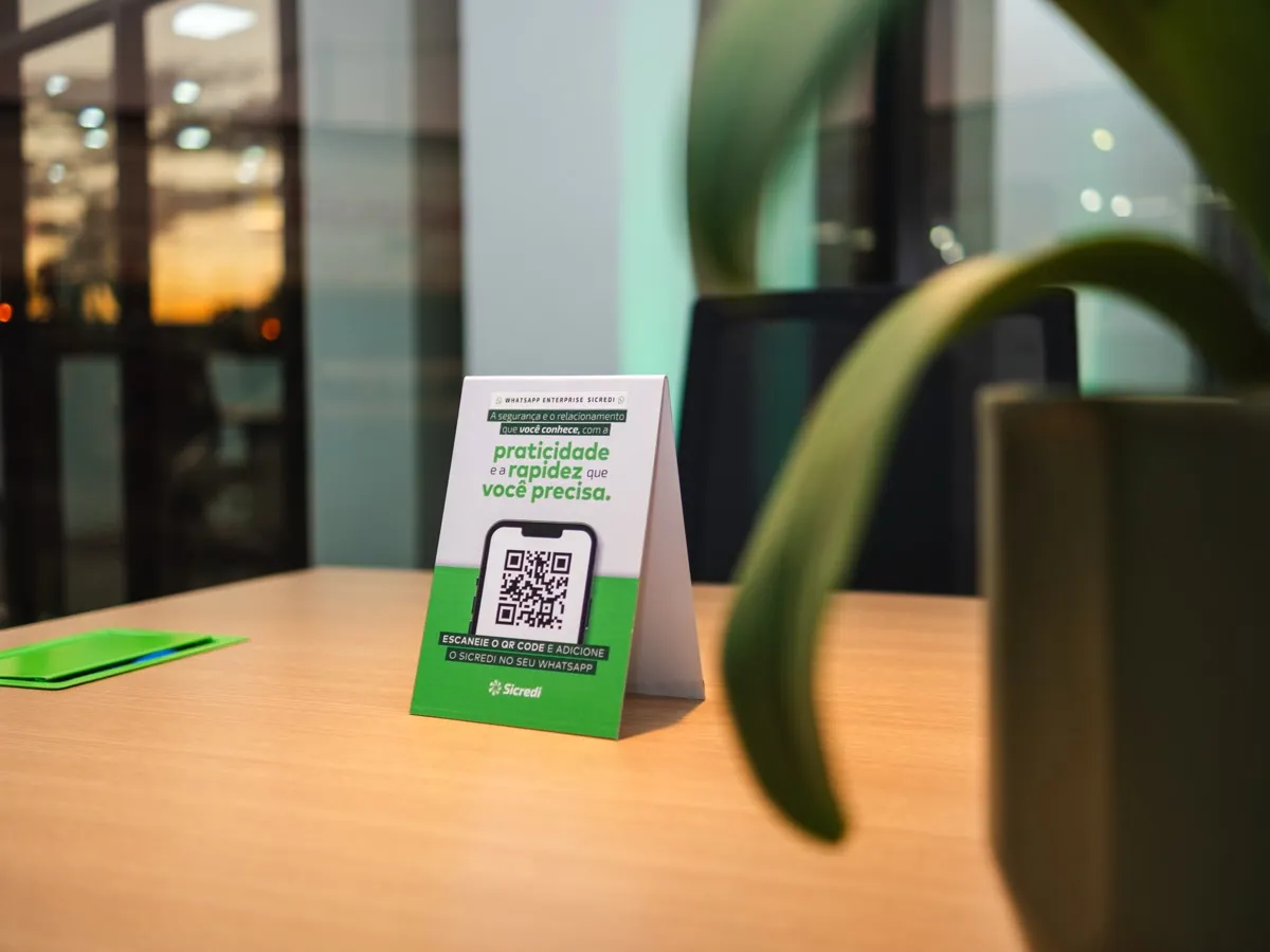 Display com QR code sobre uma mesa de madeira, com uma planta em primeiro plano